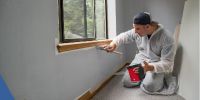 Man painting around window trim